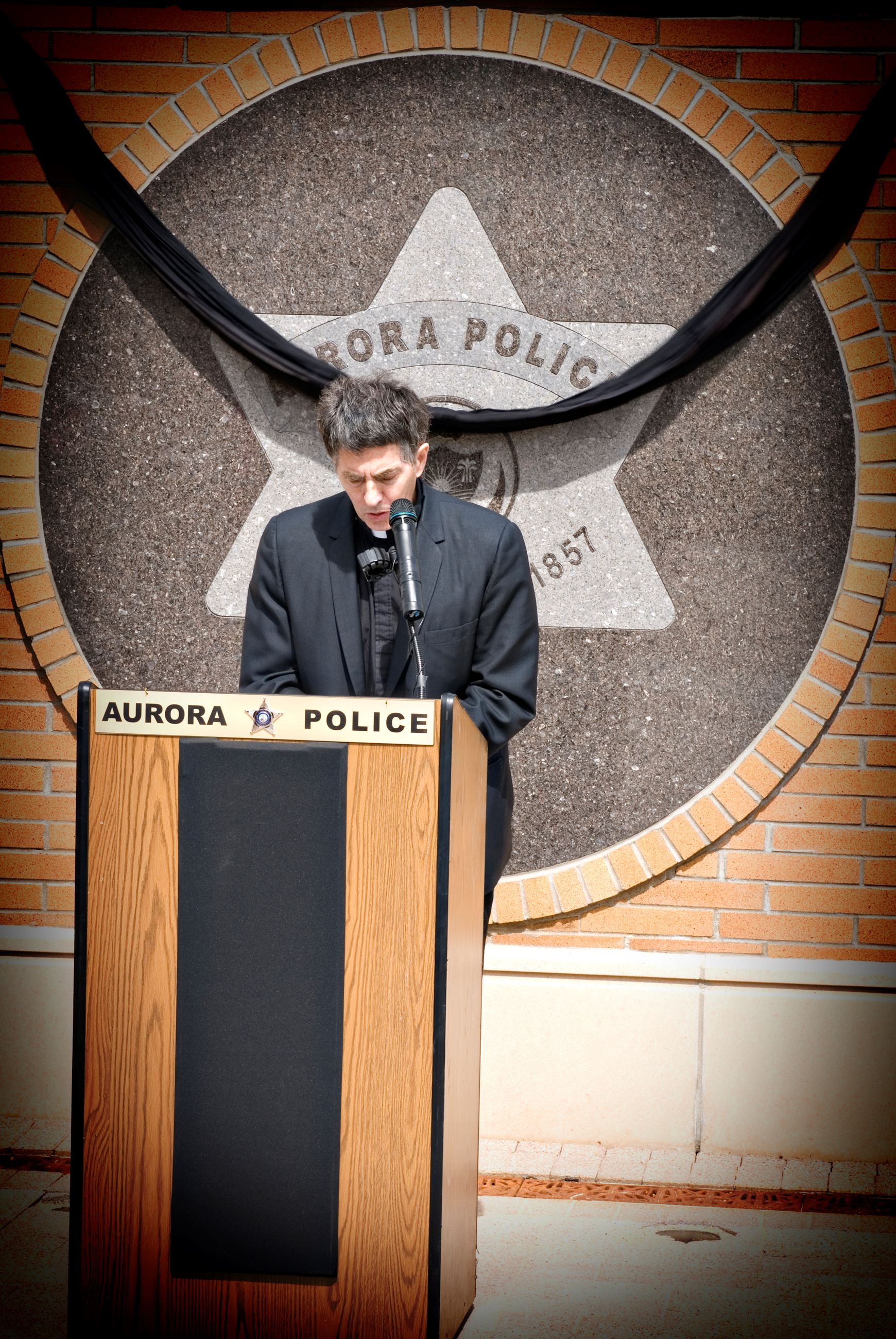 Father Jerry standing aside APD memorial wall